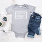 Grey baby romper that has white writing with spread love, it's the Brooklyn way. Surrounded by a white solid box.